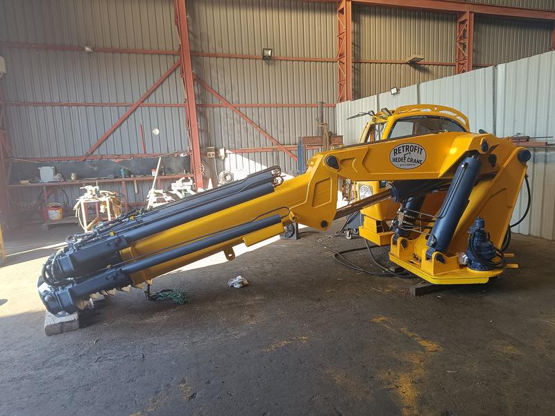 Atölyede revizyonu tamamlanmış, sarıya boyanmış katlanır bomlu vinç; bom ve silindirler yere yatırılmış, kolonda Retrofit Hedef Crane etiketi