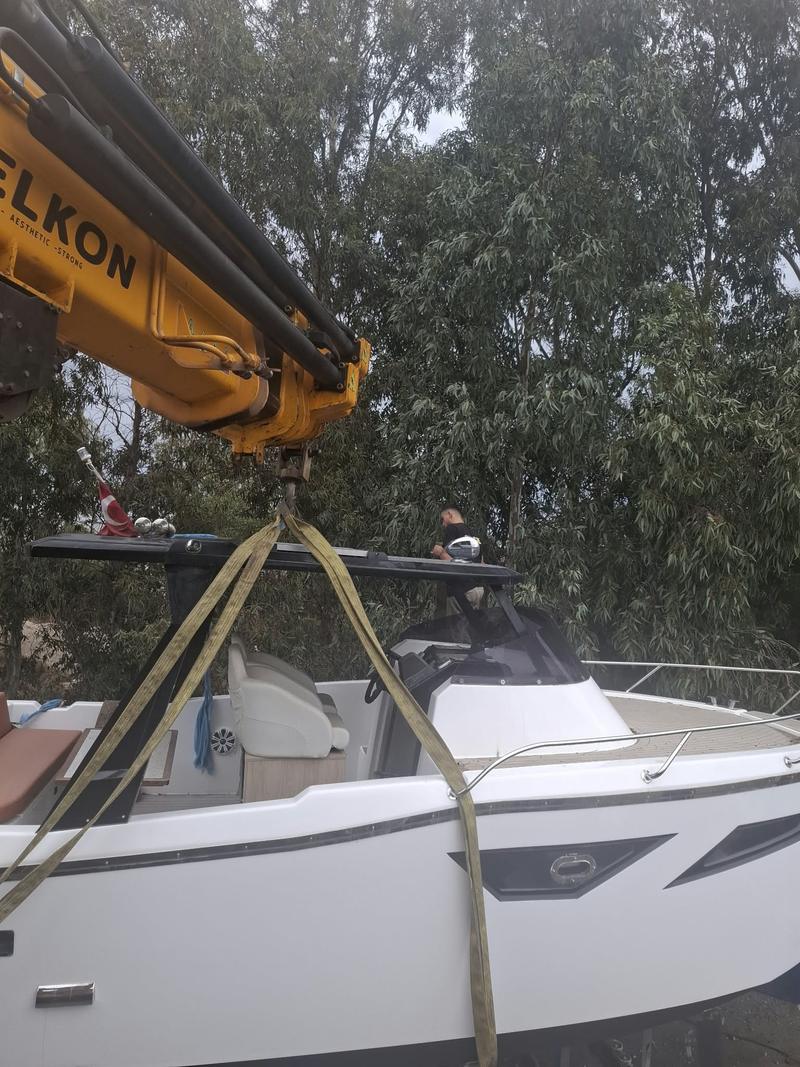 Sarı katlanır bomlu vinç sarı kaldırma kayışlarıyla beyaz bir motoryatı kaldırıyor